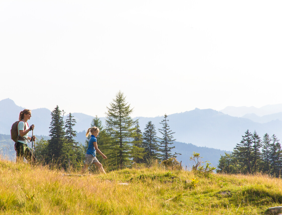 Vrouw en meisje wandelen door de bergen met op de achtergrond wat naaldbomen