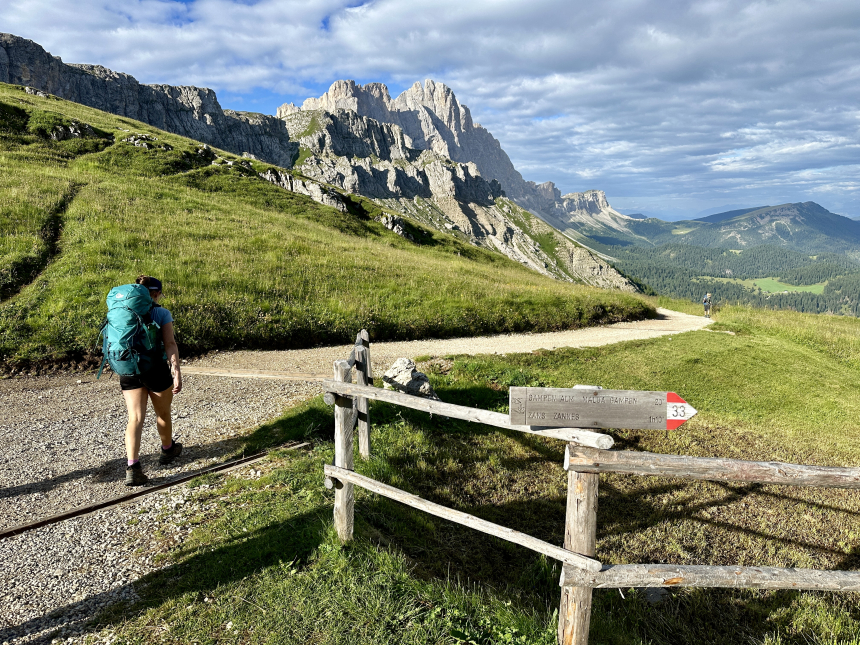 Iemand die met een grote rugzak op wegloopt van de camera, een gravelpad op naar grijze bergen toe