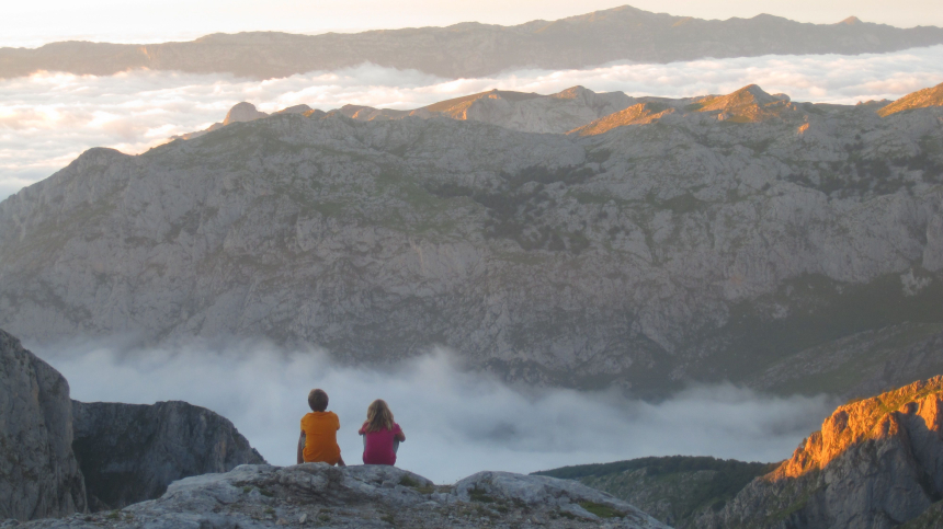 Twee kinderen die zitten te kijken naar grijze bergen met wolken ertussen